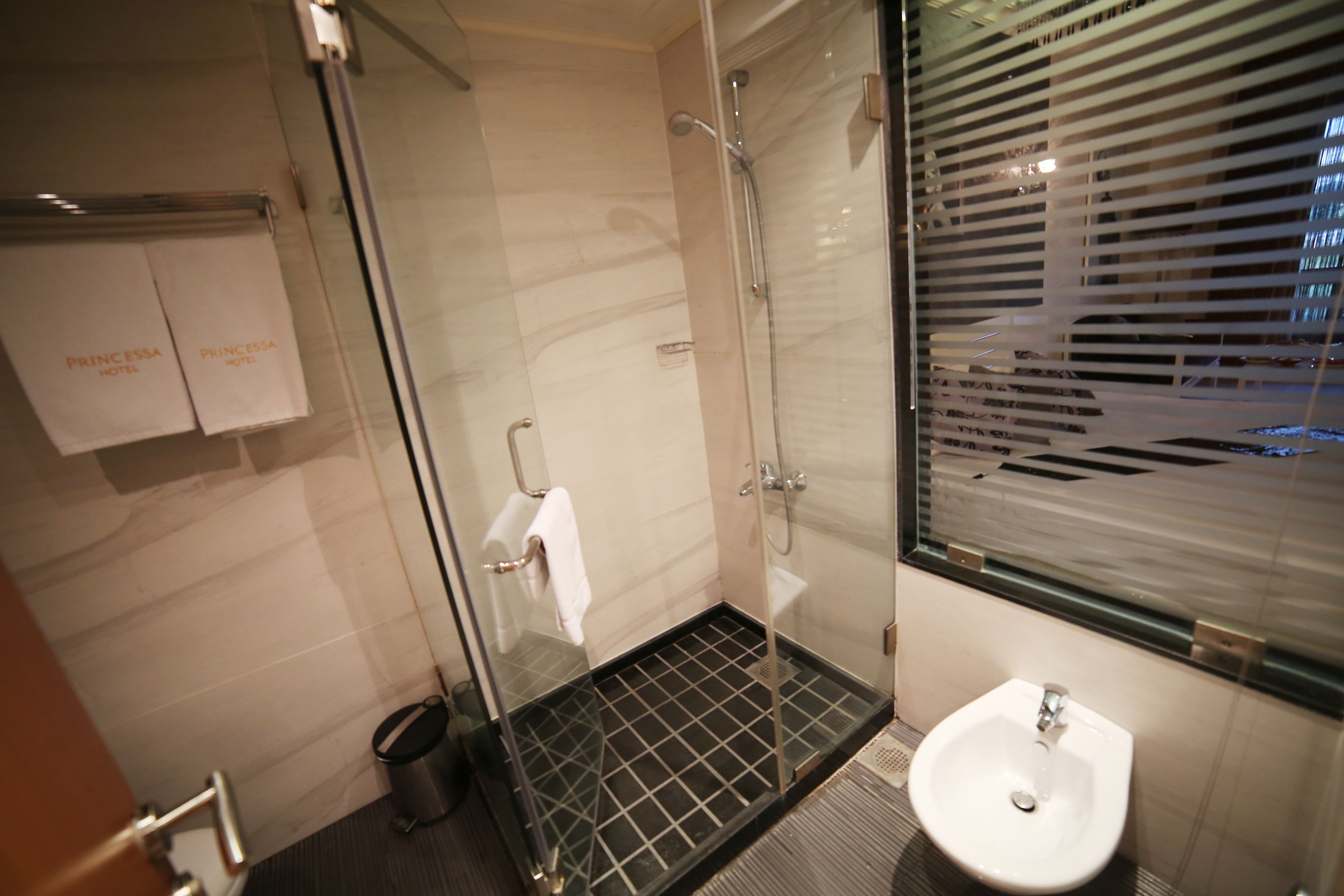 A modern bathroom with a glass shower enclosure, a white sink, and a towel rack with two towels.