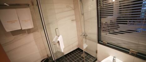 A modern bathroom with a glass shower enclosure, a white sink, and a towel rack with two towels.