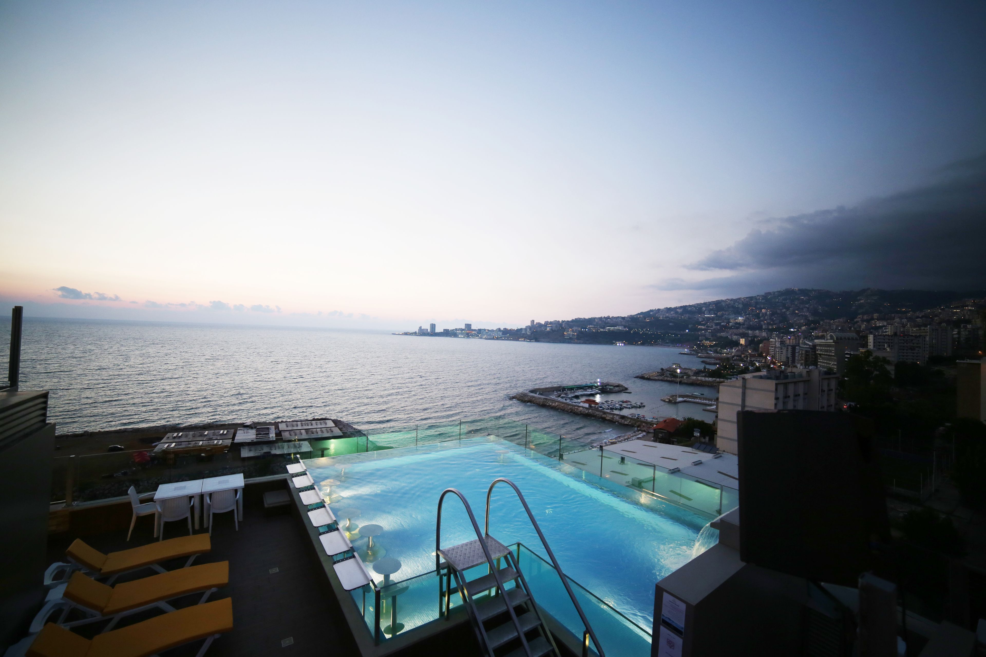 Una piscina infinita con vistas al mar y al paisaje urbano al anochecer.
