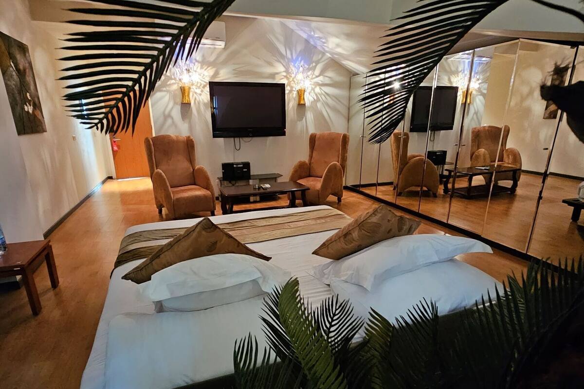 A modern bedroom with a large bed, two armchairs, a TV, and a mirror.