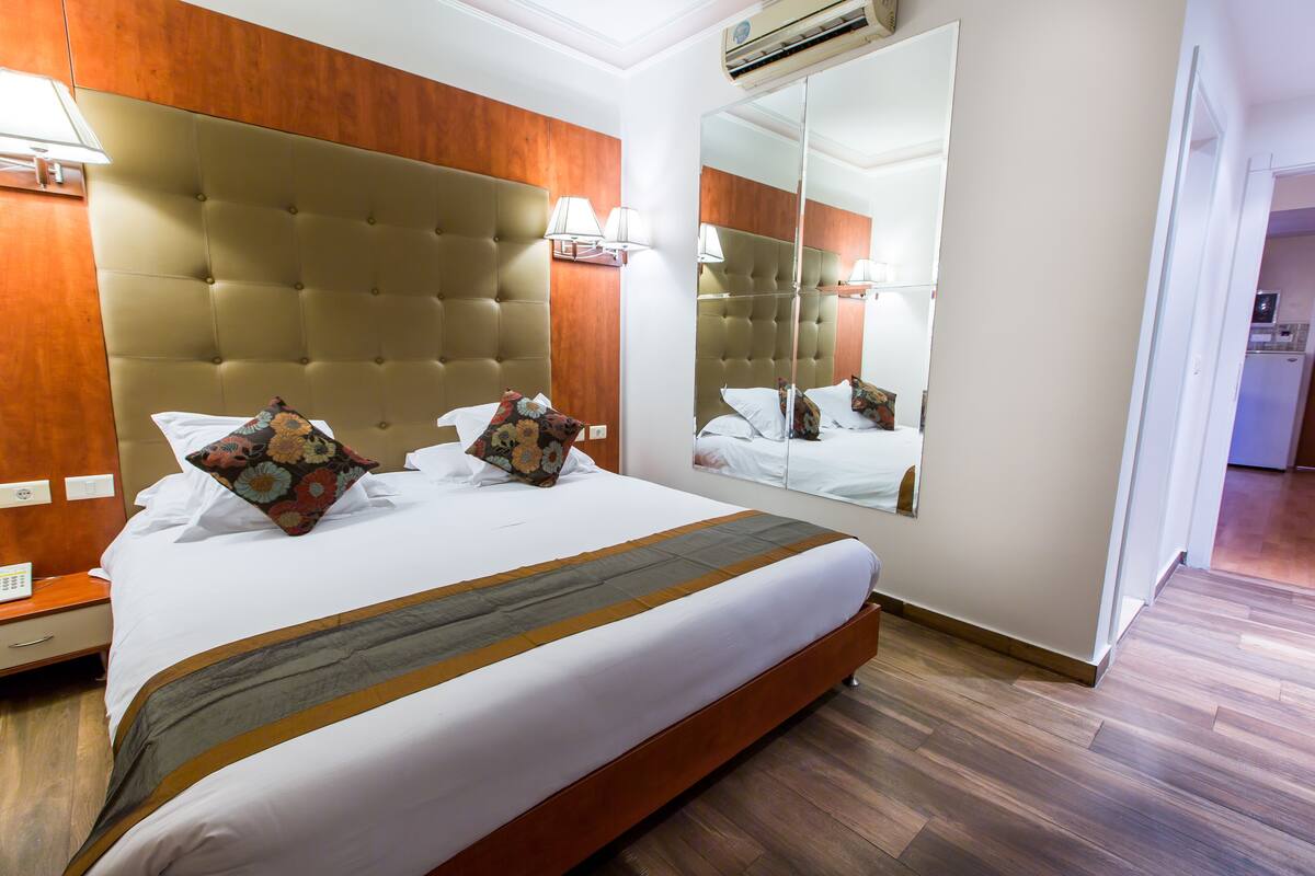 A hotel room with a large bed, a wooden headboard, a mirror, and a nightstand with a lamp.