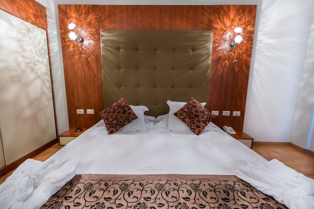 A neatly made bed with a tufted headboard, two decorative wall sconces, and a bedside table with a phone.