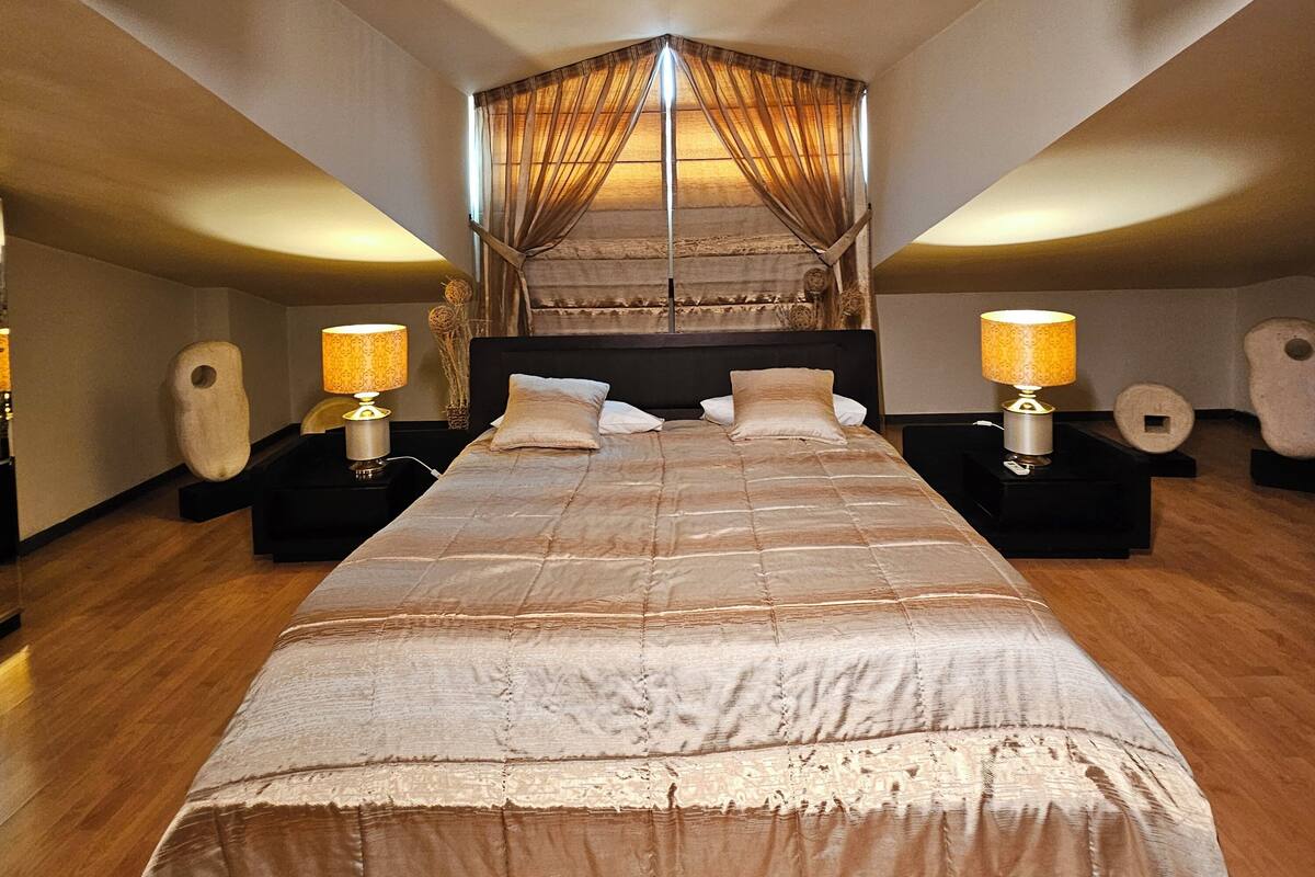 A spacious bedroom with a large bed, two bedside tables with lamps, a canopy bed, and a wooden floor.