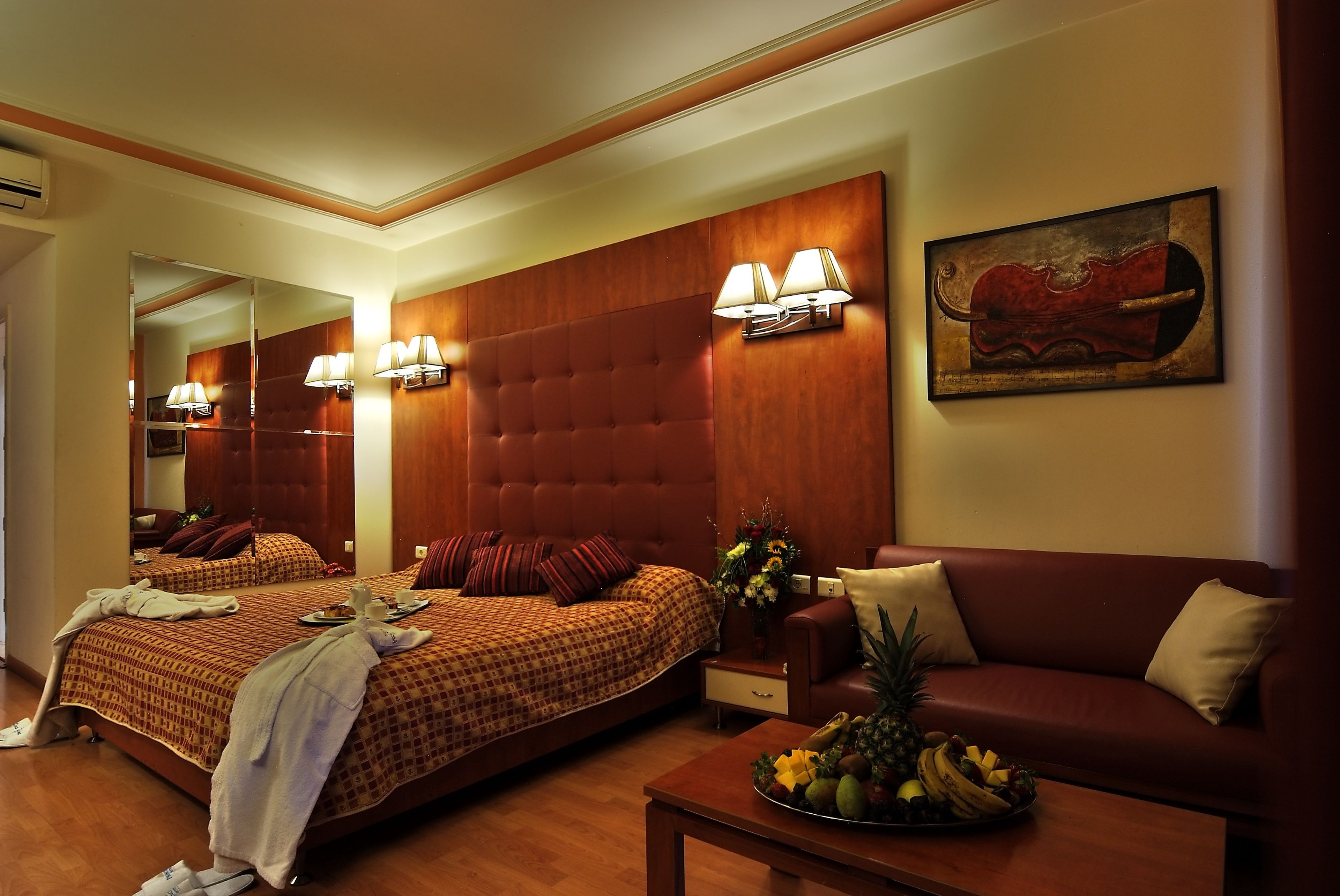 Una habitación de hotel con una cama grande, un sofá, una mesa de centro con fruta y un cuadro en la pared.