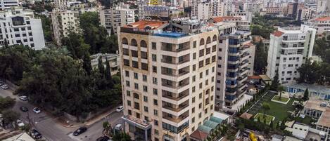 A high-rise hotel with multiple balconies, surrounded by dense urban buildings and greenery.
