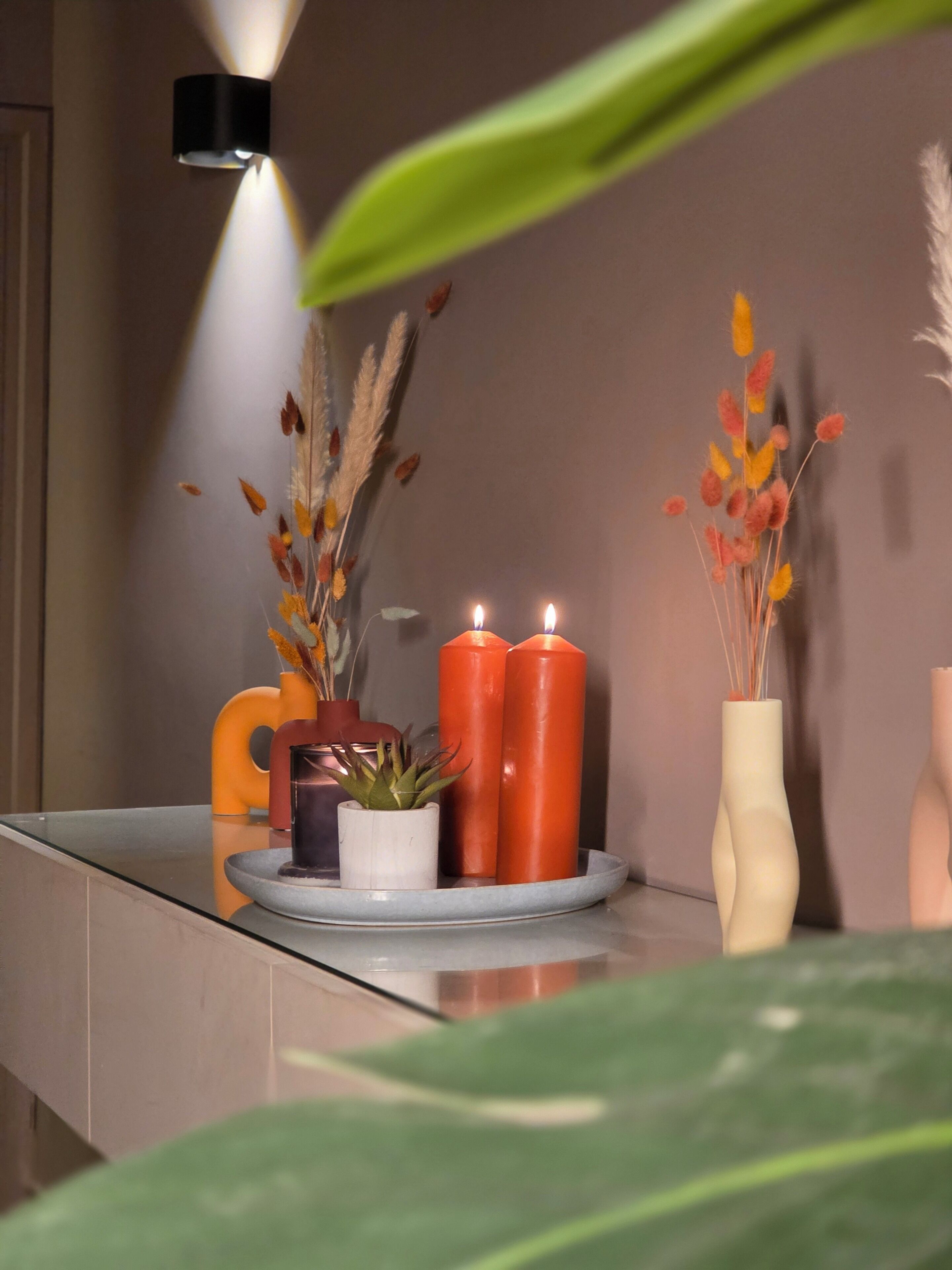 Een moderne badkamer met een glazen douchecabine, een witte wastafel en een spiegel. Op een dienblad staan twee kaarsen, een potplant en decoratief gras.