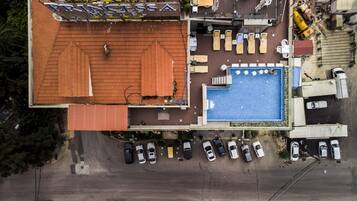 Vista aérea de un hotel con piscina, sillas de descanso y un área de estar al aire libre cubierta.