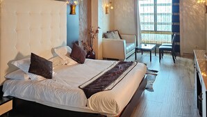 Une chambre spacieuse avec un grand lit, un coin salon avec un canapé et des fauteuils, et un lustre.