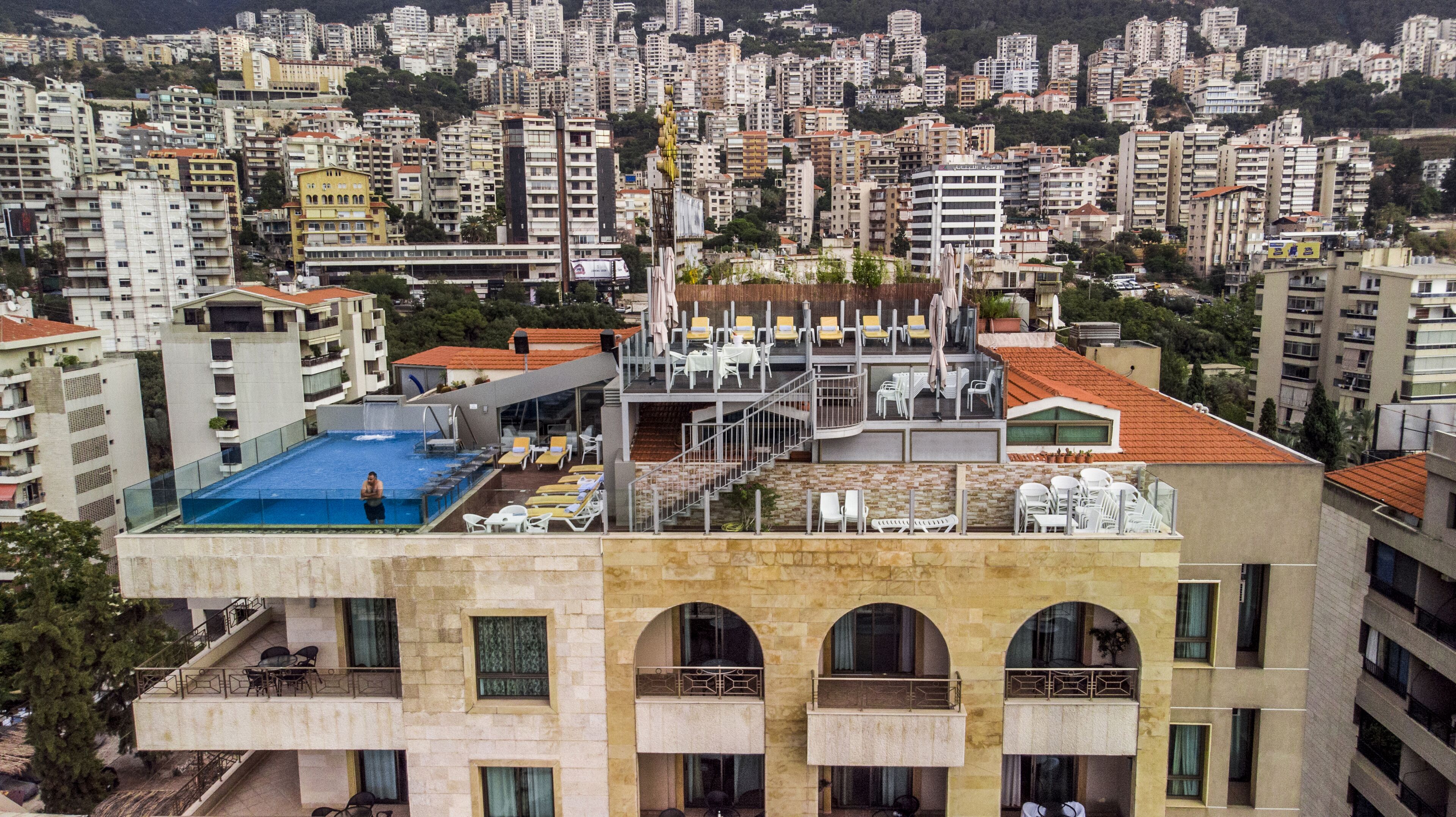 A high-rise building with a rooftop pool, multiple balconies, and a view of a densely populated cityscape.