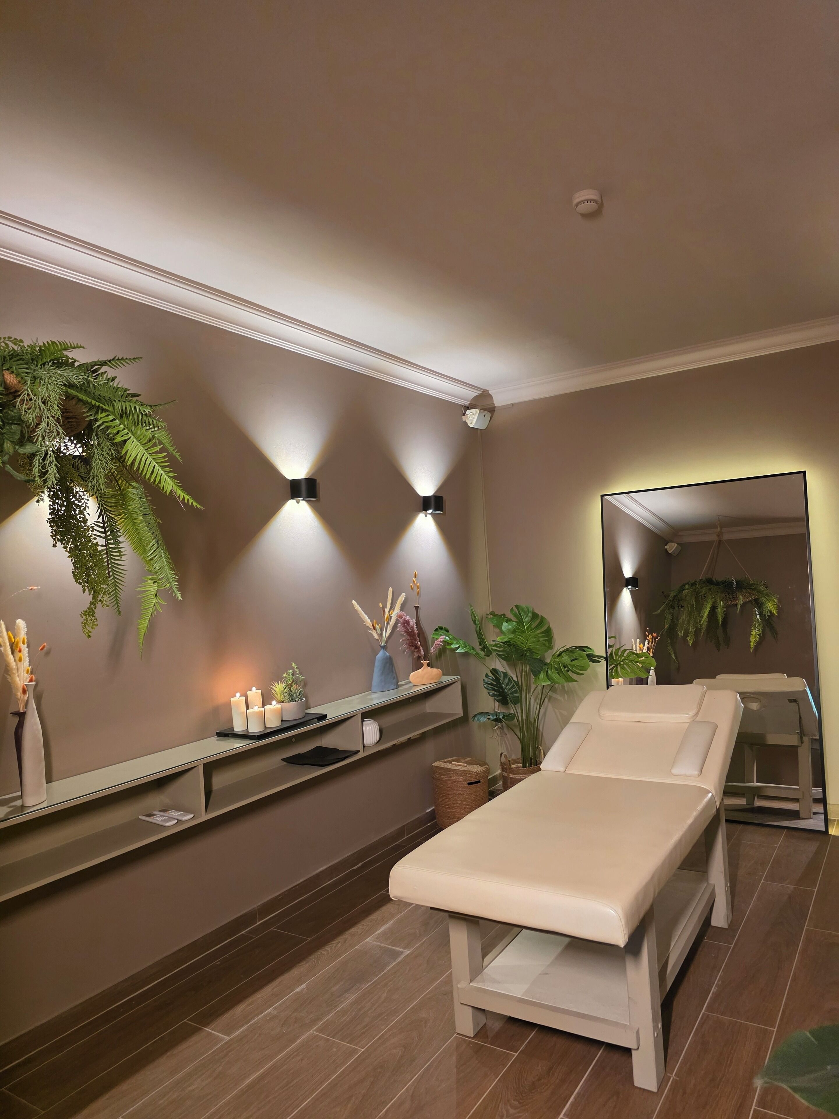 A spa room with a massage table, wall-mounted shelves with decorative items, and large potted plants.