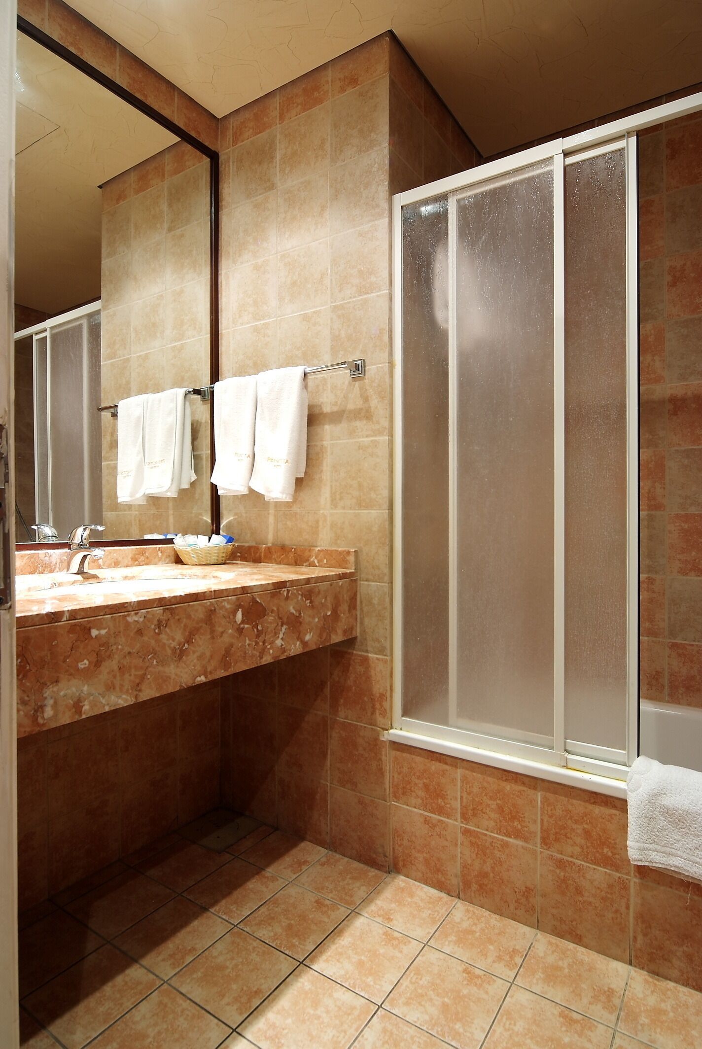 A bathroom with a marble sink, a mirror, a towel rack with towels, and a glass shower enclosure.