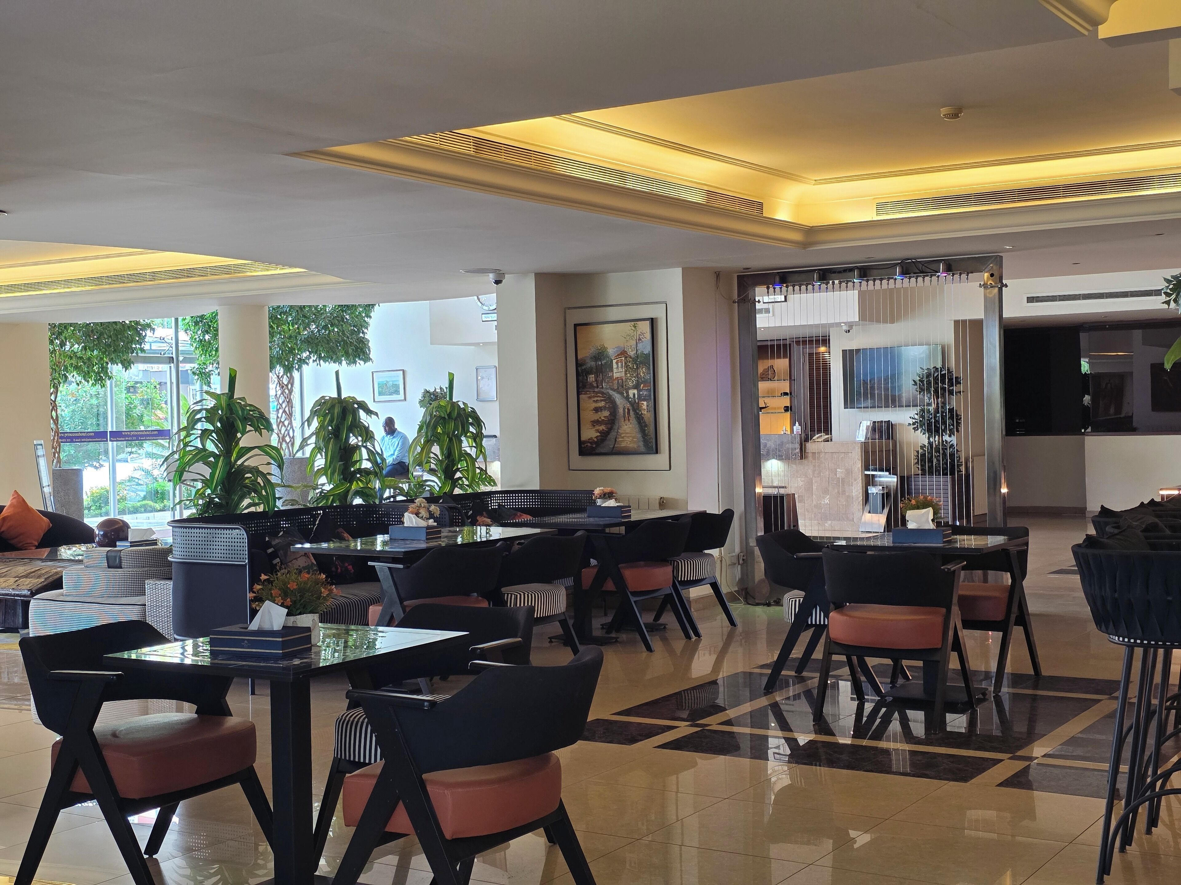A modern hotel lobby with a mix of seating options, including tables and chairs, and a large window offering a view of the outdoors.