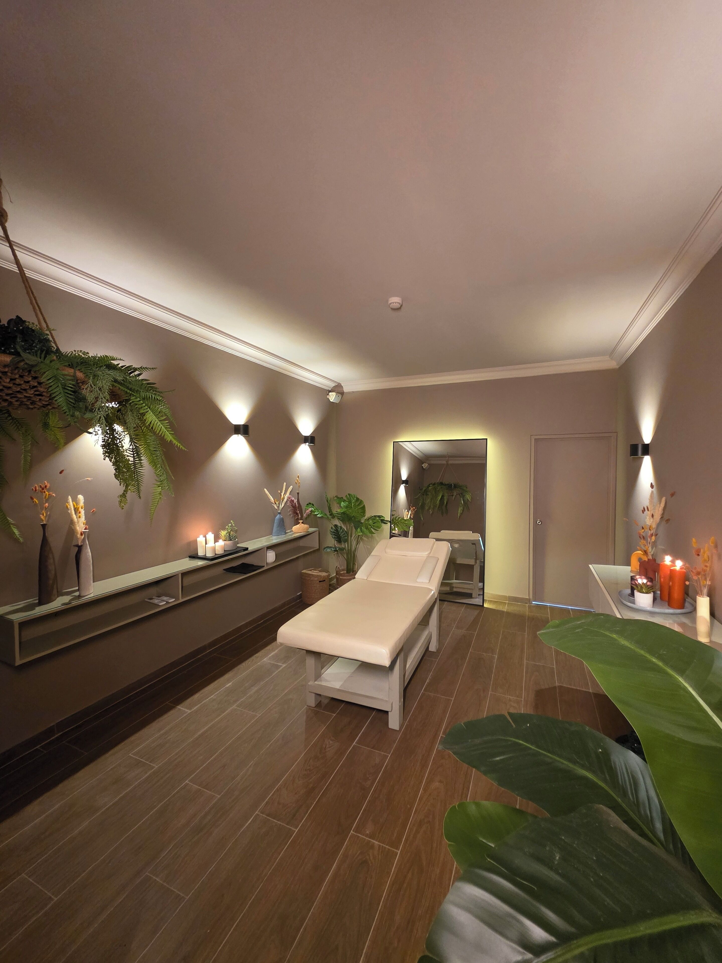 Ein moderner Wellnessraum mit Massagetisch, Pflanzen und Wandbeleuchtung.