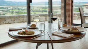 Una mesa de comedor con platos de comida, copas de vino y vistas al campo a través de grandes ventanales.