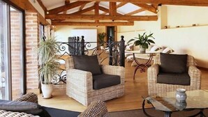 Una habitación acogedora con muebles de mimbre, una mesa de vidrio y vistas a un muro de ladrillo.
