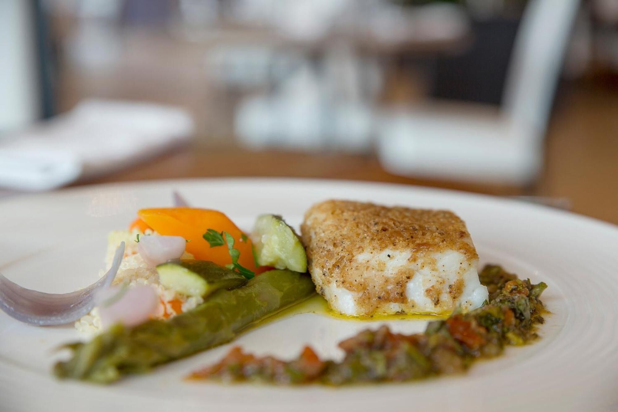 A plate with a piece of fish, a grilled vegetable, and a small portion of sauce.