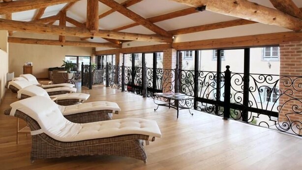 Una habitación soleada con sillones de mimbre, una mesita y un balcón con barandillas de hierro forjado.