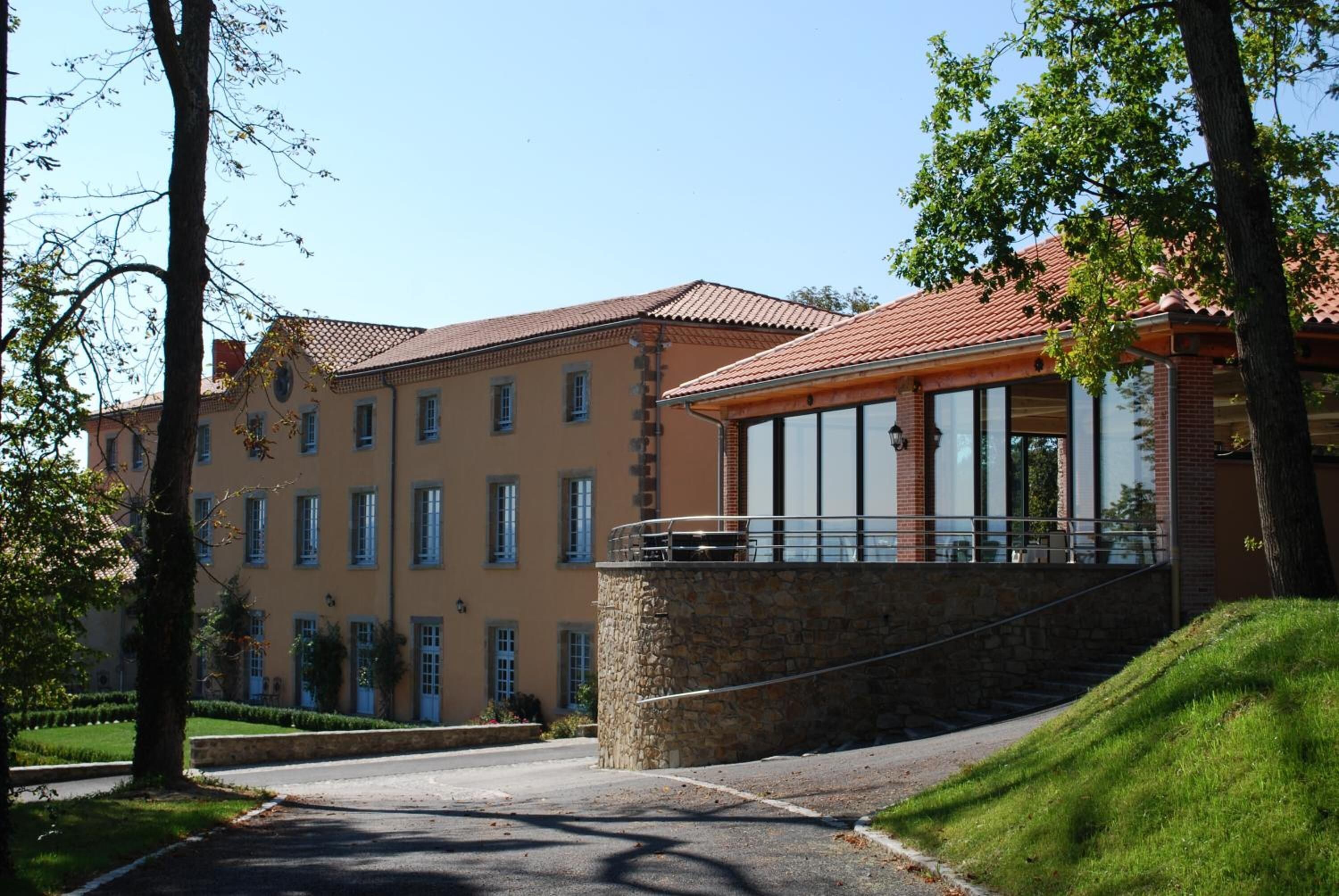 A building with a stone base and a red-tiled roof, featuring large windows and a balcony.