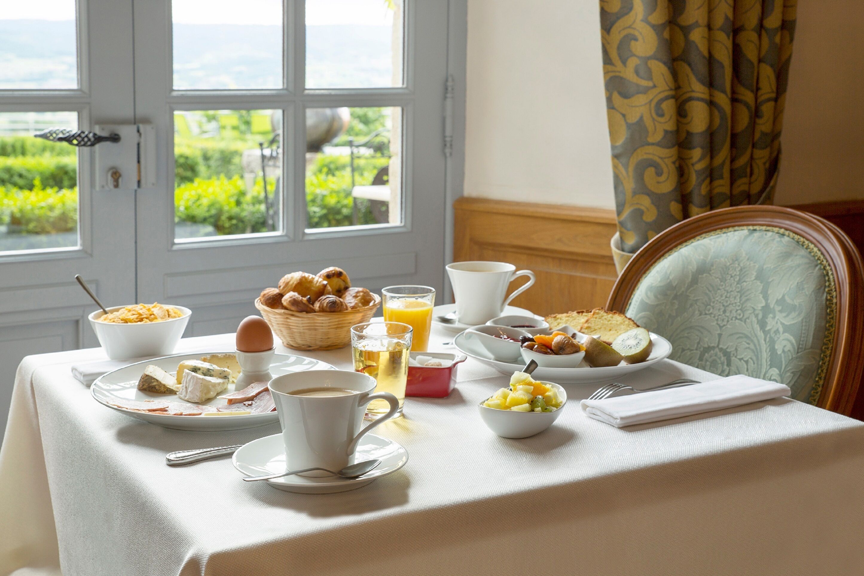 Una mesa de desayuno con diferentes platos, una taza de café y vistas al exterior de vegetación.