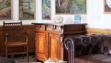 A room with a leather sofa, a wooden chair, a glass coffee table with teapots, and a cabinet. Three large paintings adorn the wall.