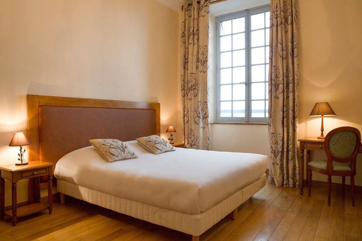 A hotel room with a large bed, two bedside lamps, a chair, and a window with curtains.