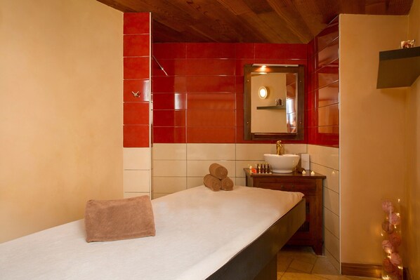 A bathroom with a wooden ceiling, a white sink, and a mirror above it. There are towels on the counter and a small shelf with toiletries.