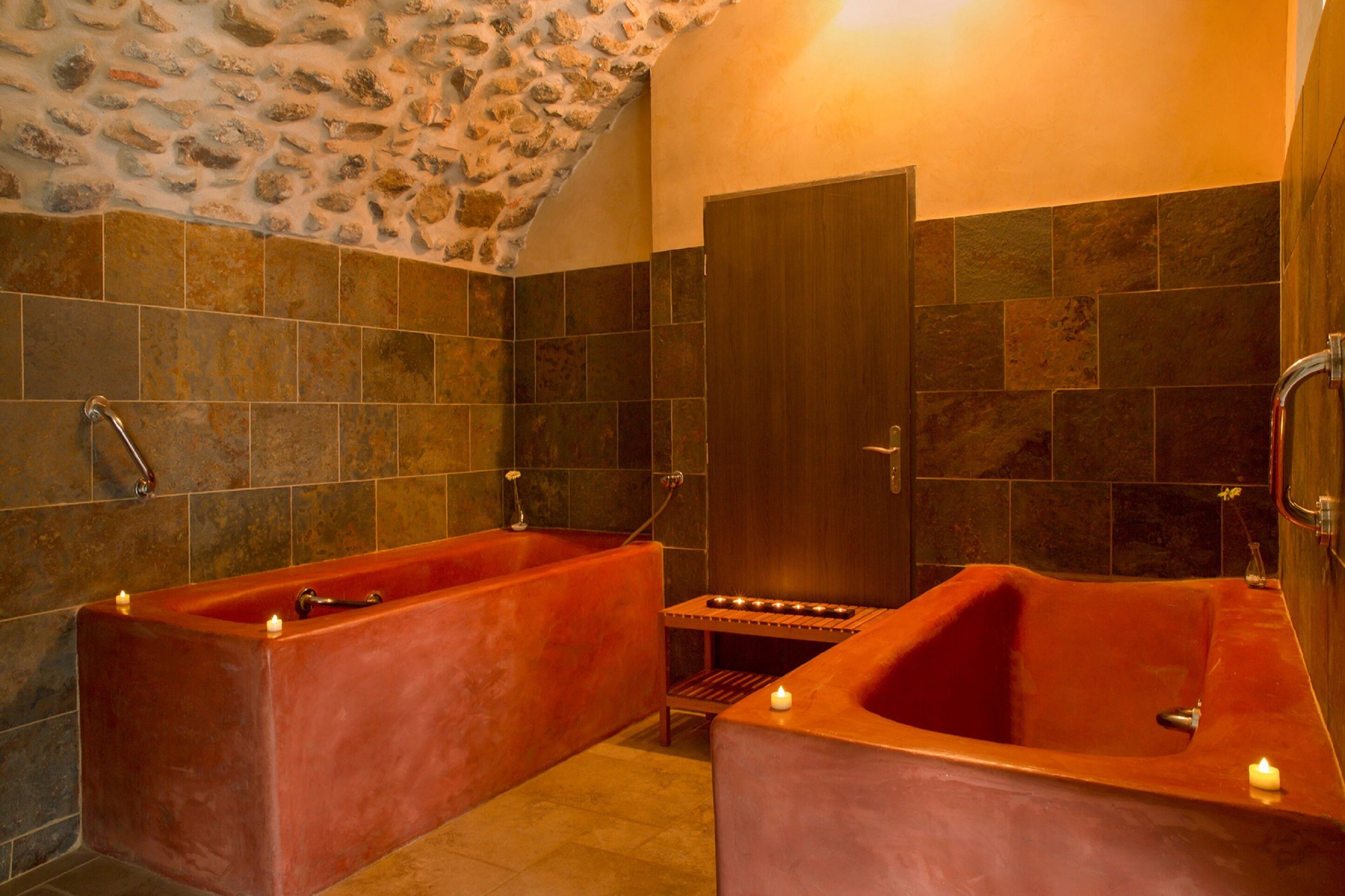 Un baño con dos tinas rojas grandes y rectangulares, un estante pequeño y una puerta.