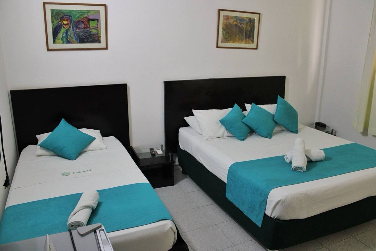 Two twin beds with teal bedding, a black headboard, and a white wall with two framed artworks.