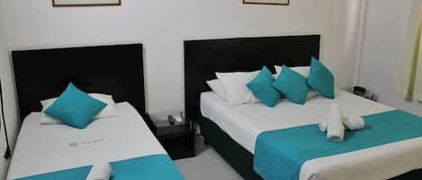 Dos camas individuales con ropa de cama color turquesa, un cabecero negro y una pared blanca decorada con dos cuadros enmarcados.