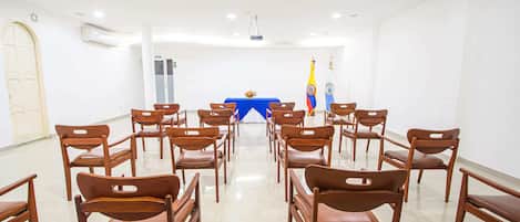 A conference room with rows of wooden chairs facing a blue table with flags.