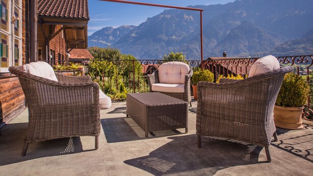 A terrace with wicker furniture and a view of mountains. - Gasthof Schoenegg (Ringgenberg)