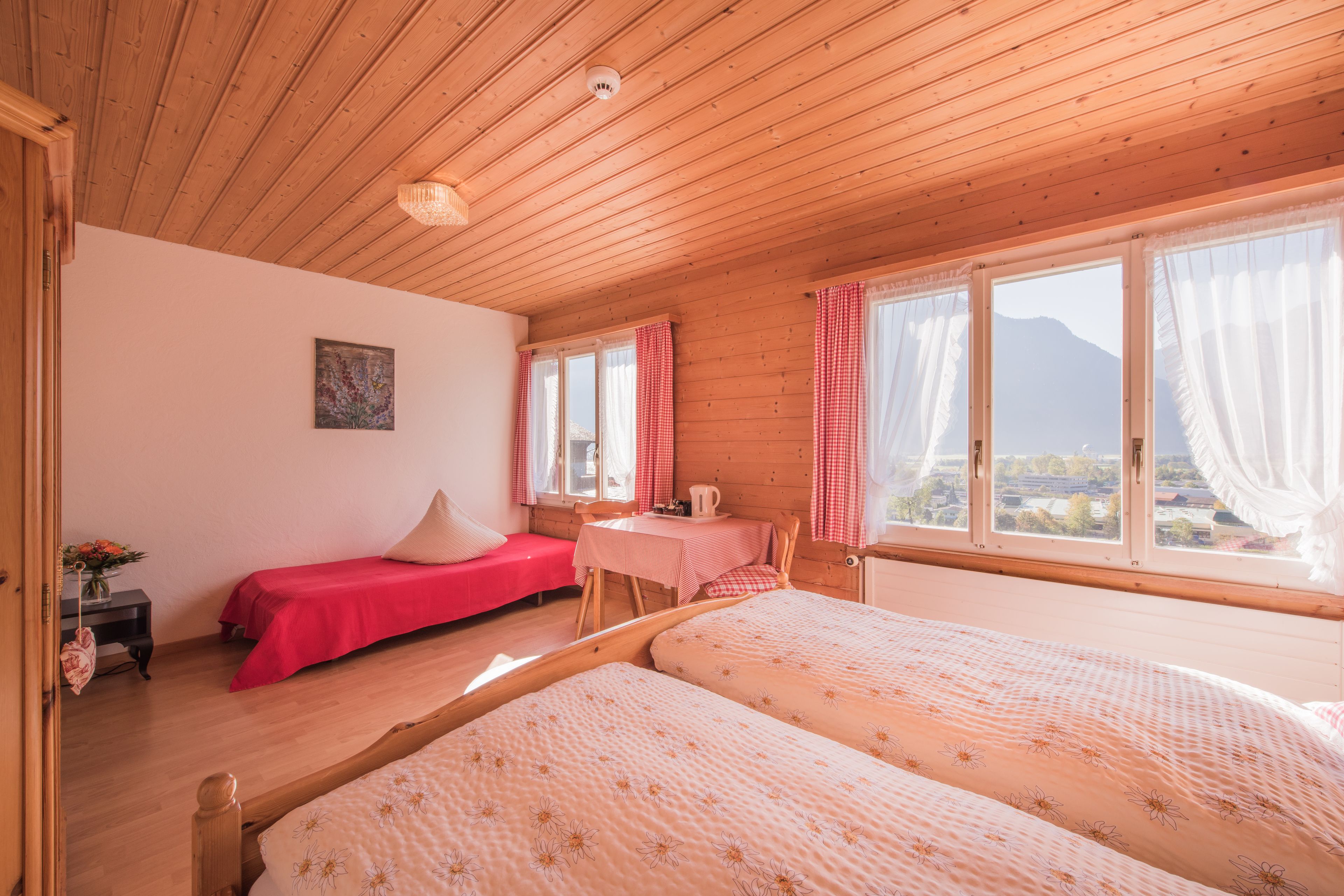 A cozy room with wooden ceilings, two beds, a small table, and a window with curtains.