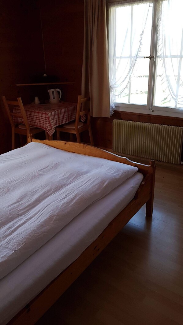 Una cama de madera en una habitación con una mesa, sillas, un radiador y una ventana con cortinas.