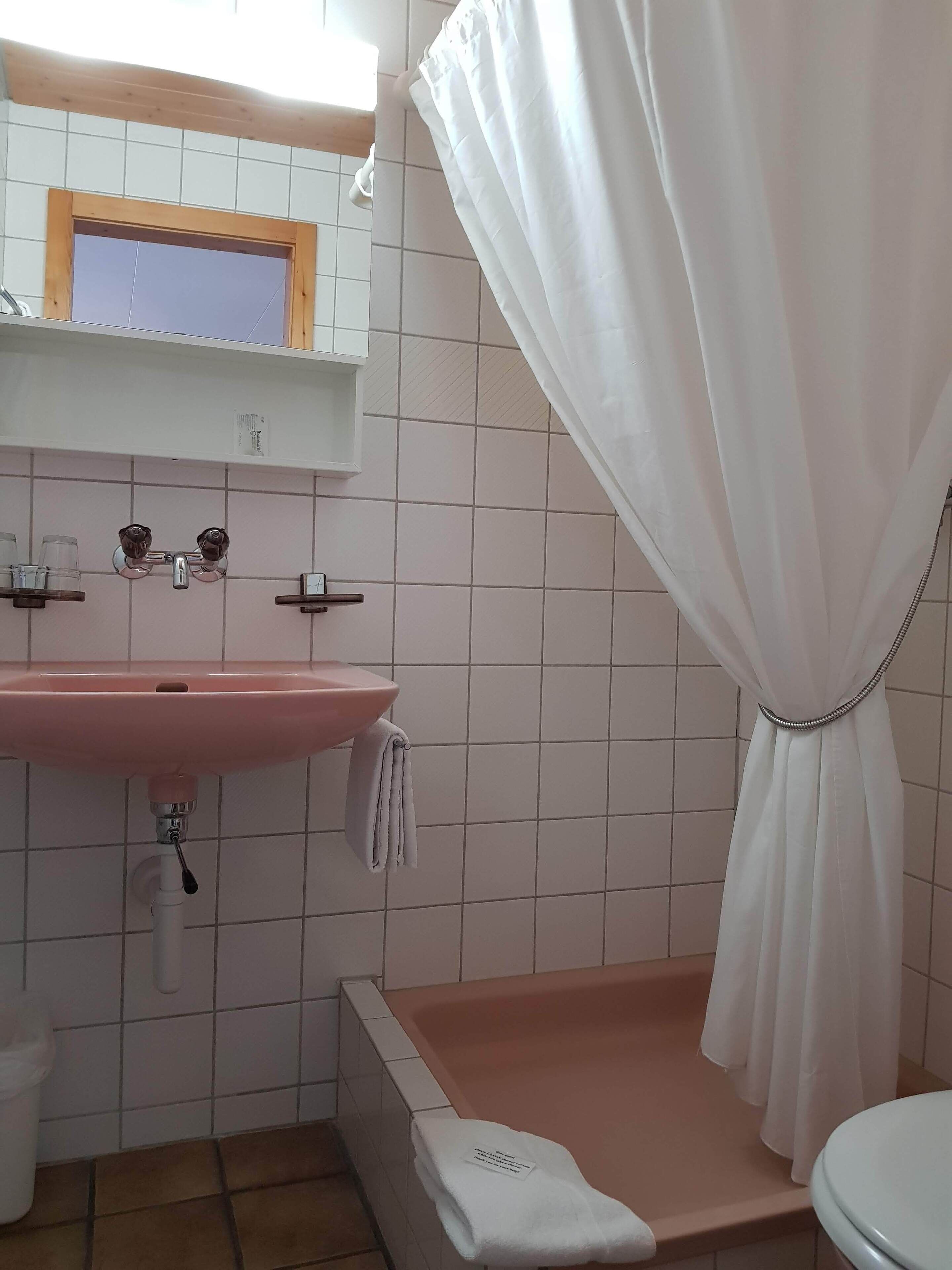 A bathroom with a pink sink, a white bathtub, and a shower curtain.