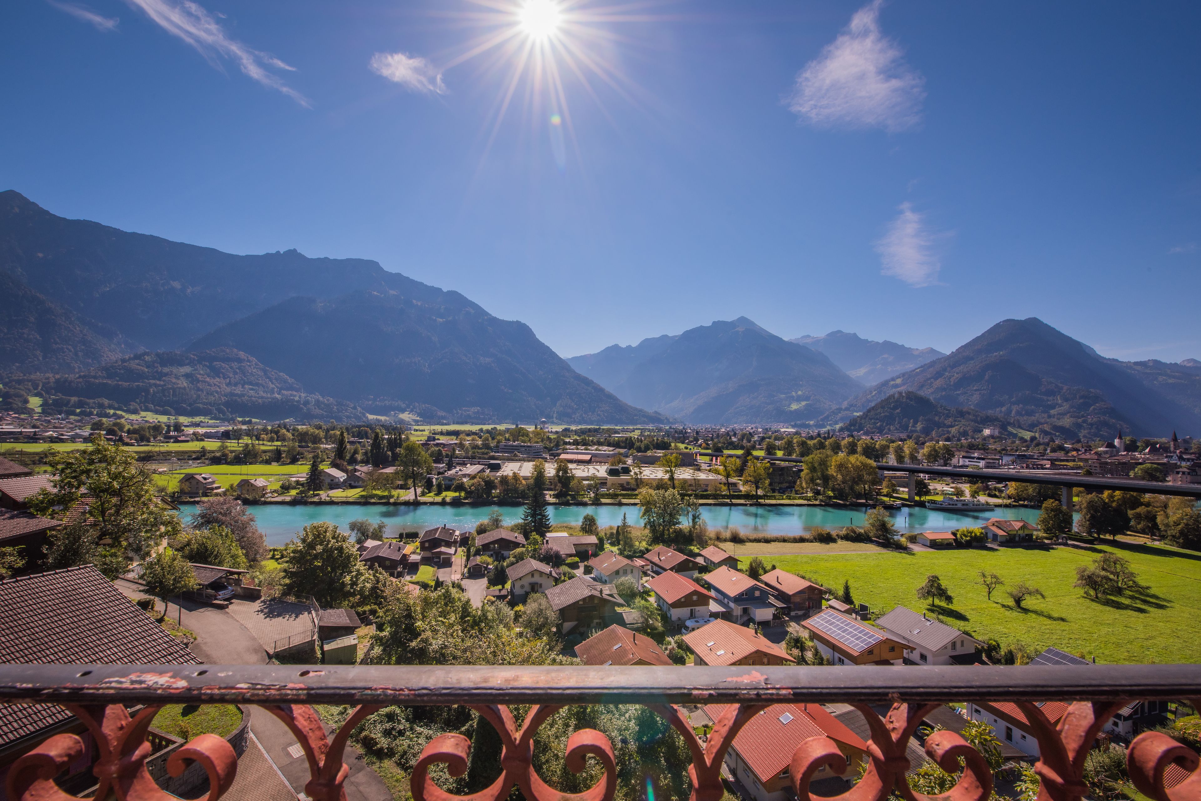 Una vista panorámica de un pueblo de montaña con un río, casas y montañas al fondo.