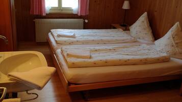 Une chambre avec deux lits, un plancher en bois, une fenêtre avec des rideaux rouges, un radiateur et un lavabo.