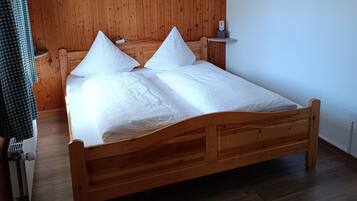 Una cama de madera con cabecera, ropa de cama blanca y una mesita de noche con lámpara.