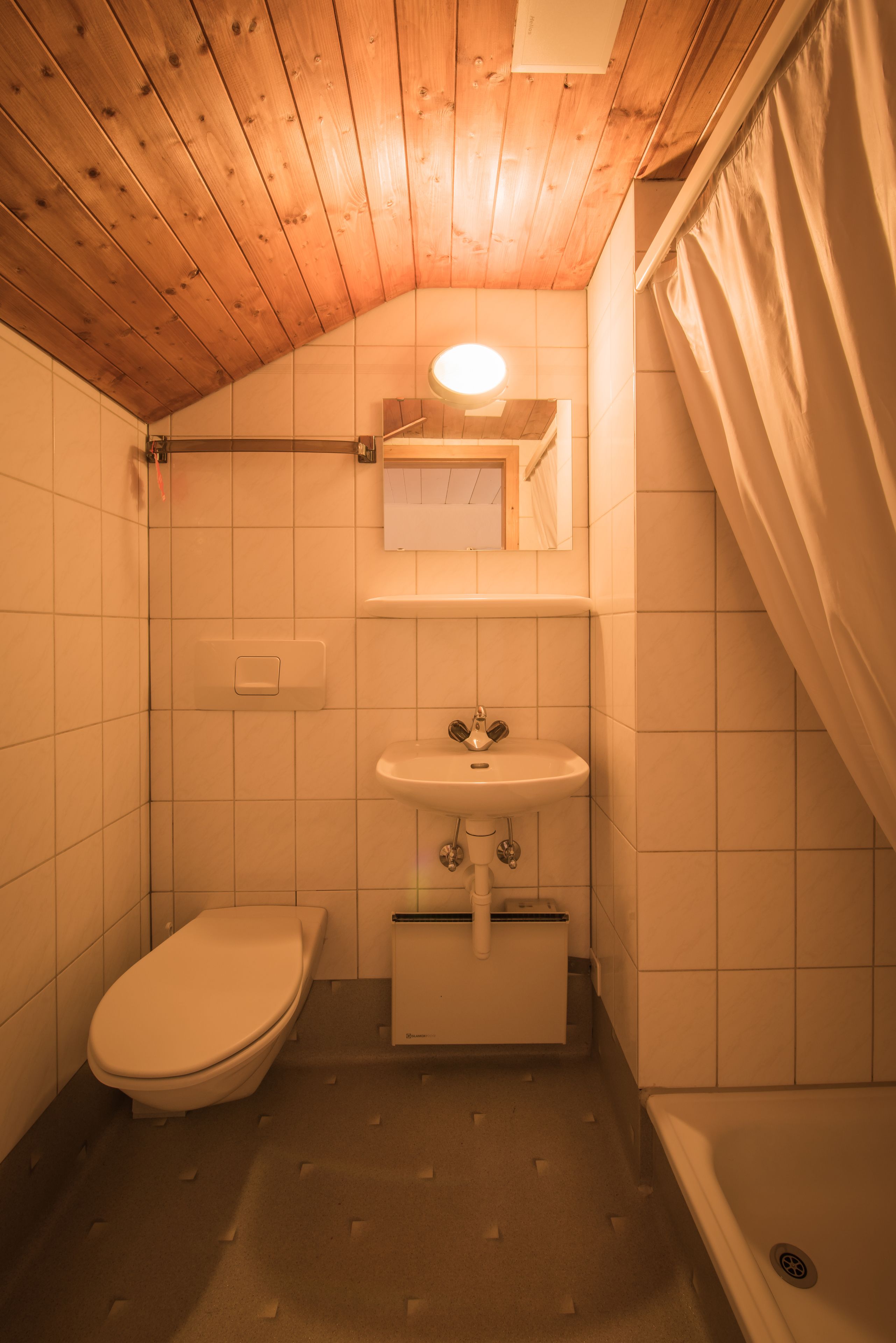 Une petite salle de bain compacte avec un plafond en bois, des toilettes, un lavabo et un espace douche.