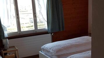 A bedroom with a large bed, a bedside table, a lamp, and a window with curtains.