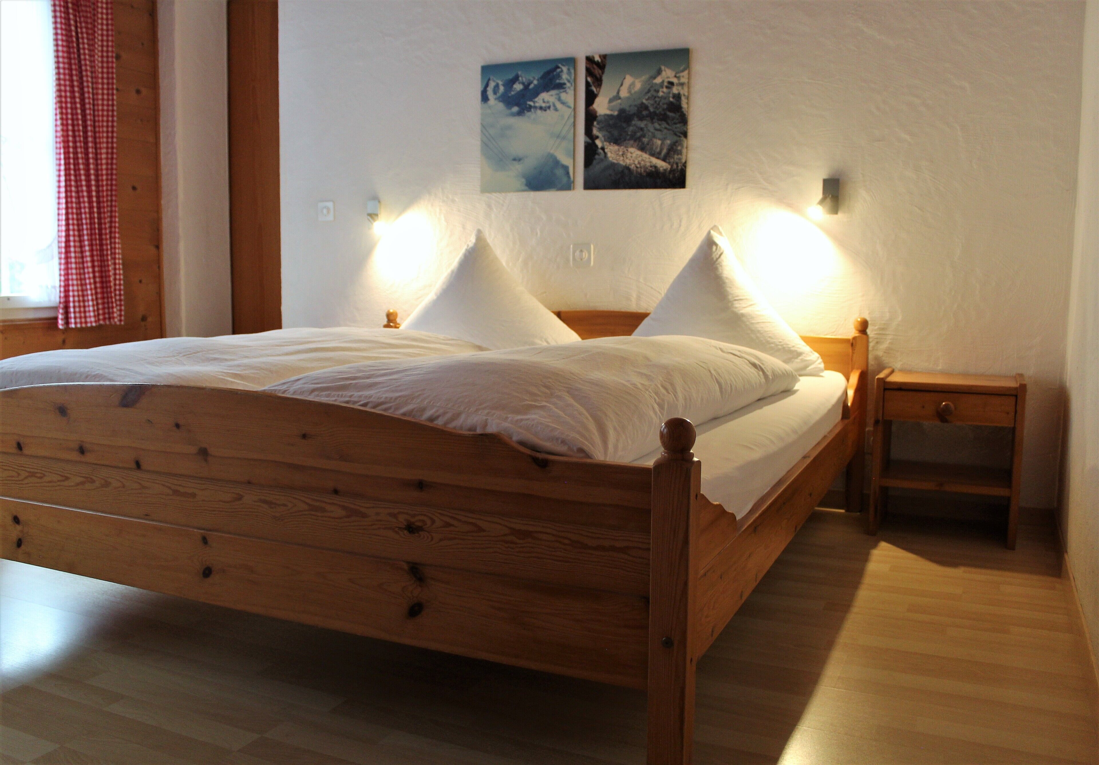 A wooden bed with two pillows, a nightstand, and a wall-mounted light fixture.