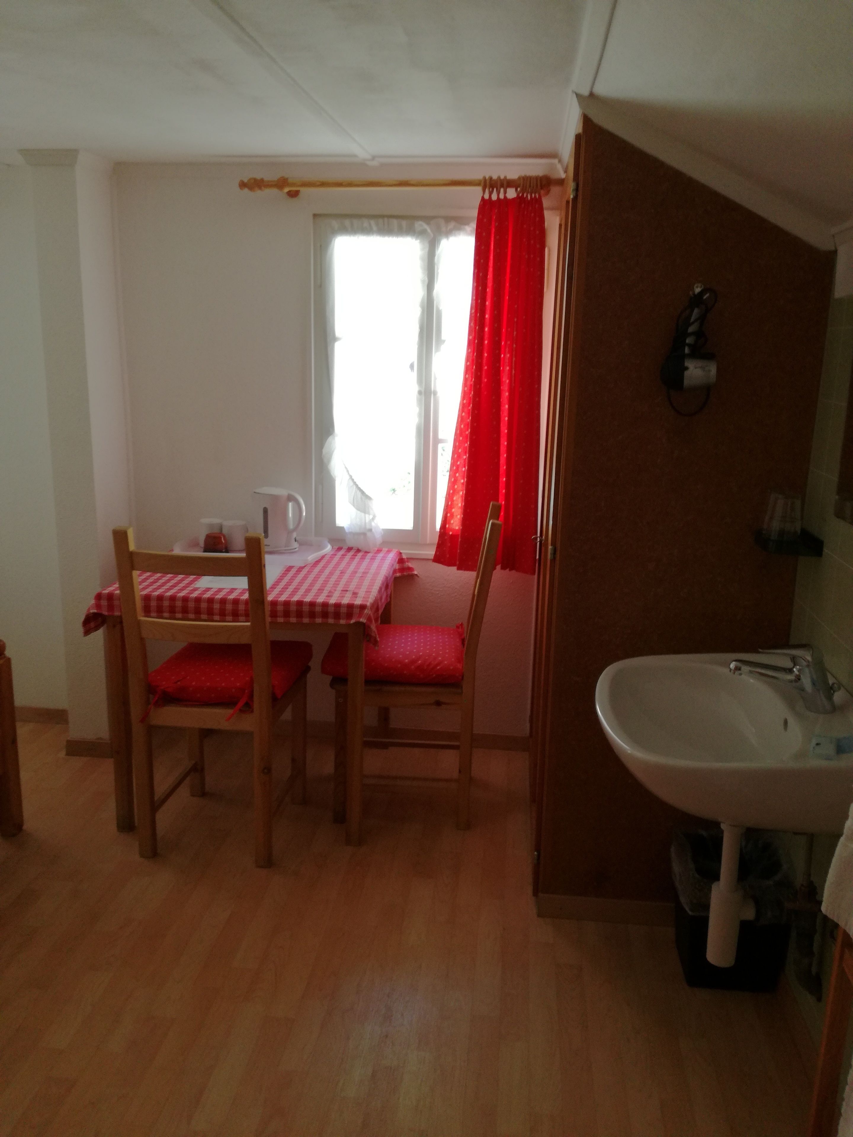 Quarto compacto com uma mesa de jantar e cadeiras, uma janela com cortinas e uma pia.