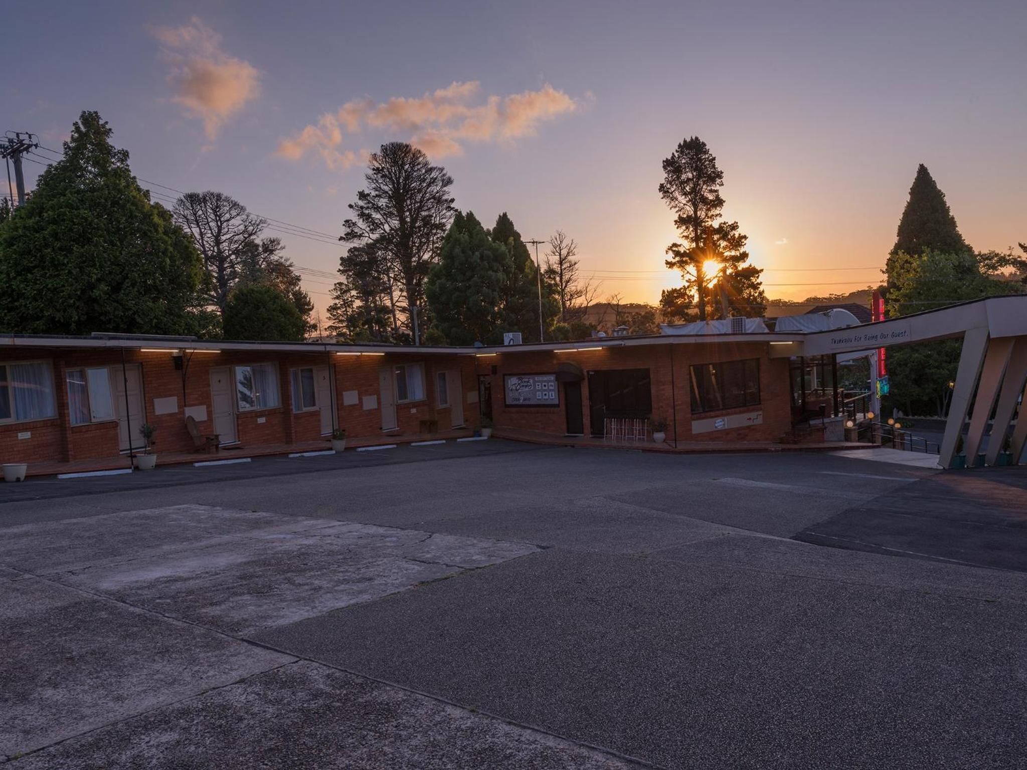 Ein Motel mit mehreren Zimmern, einem Parkplatz und einem Gebäude mit der Aufschrift 'Motel für Ihren Besuch'.