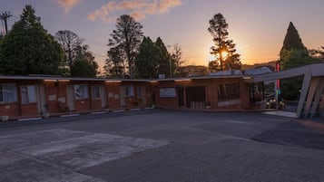 Ein Motel mit mehreren Zimmern, einem Parkplatz und einem Gebäude mit der Aufschrift 'Motel für Ihren Besuch'.