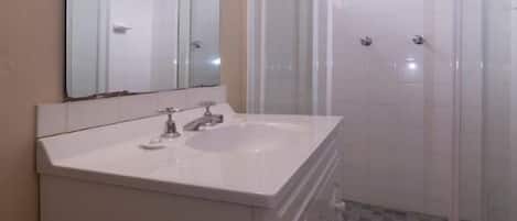 A bathroom with a white sink, mirror, and shower enclosure.