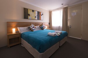 A hotel room with a bed, a nightstand, a wall-mounted artwork, a door, and a window with curtains.