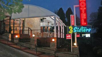 A motel with a neon sign for '3 Sisters' and a 'Motel Restaurant' sign.
