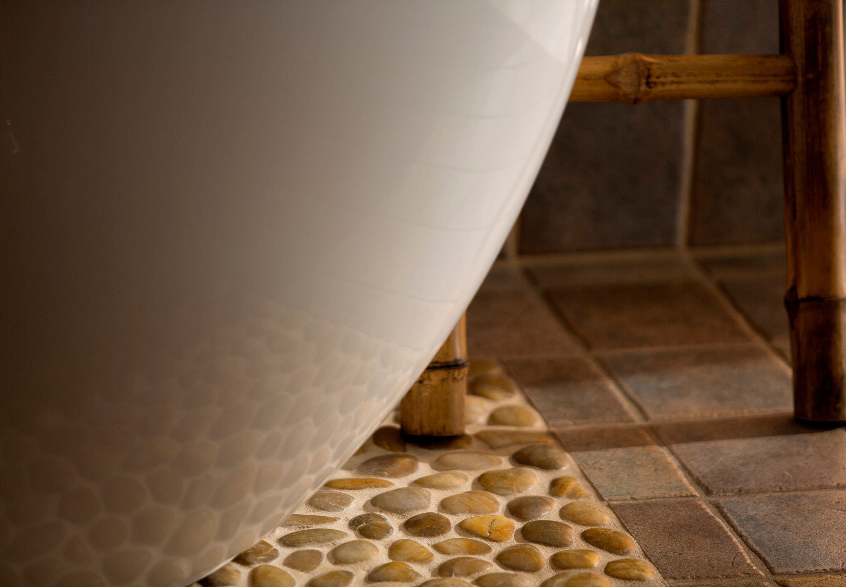 A bathtub with a textured surface, bamboo legs, and a pebble-patterned floor.
