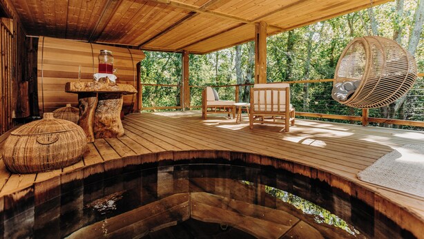A wooden deck with a hot tub, wooden furniture, and a hanging chair. - Les Frères Ibarboure (Bidart)
