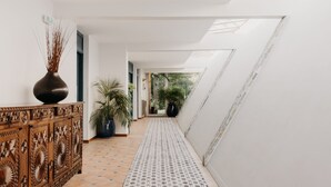 A corridor with patterned flooring, a wooden cabinet with a vase, and potted plants. - Les Frères Ibarboure (Bidart)