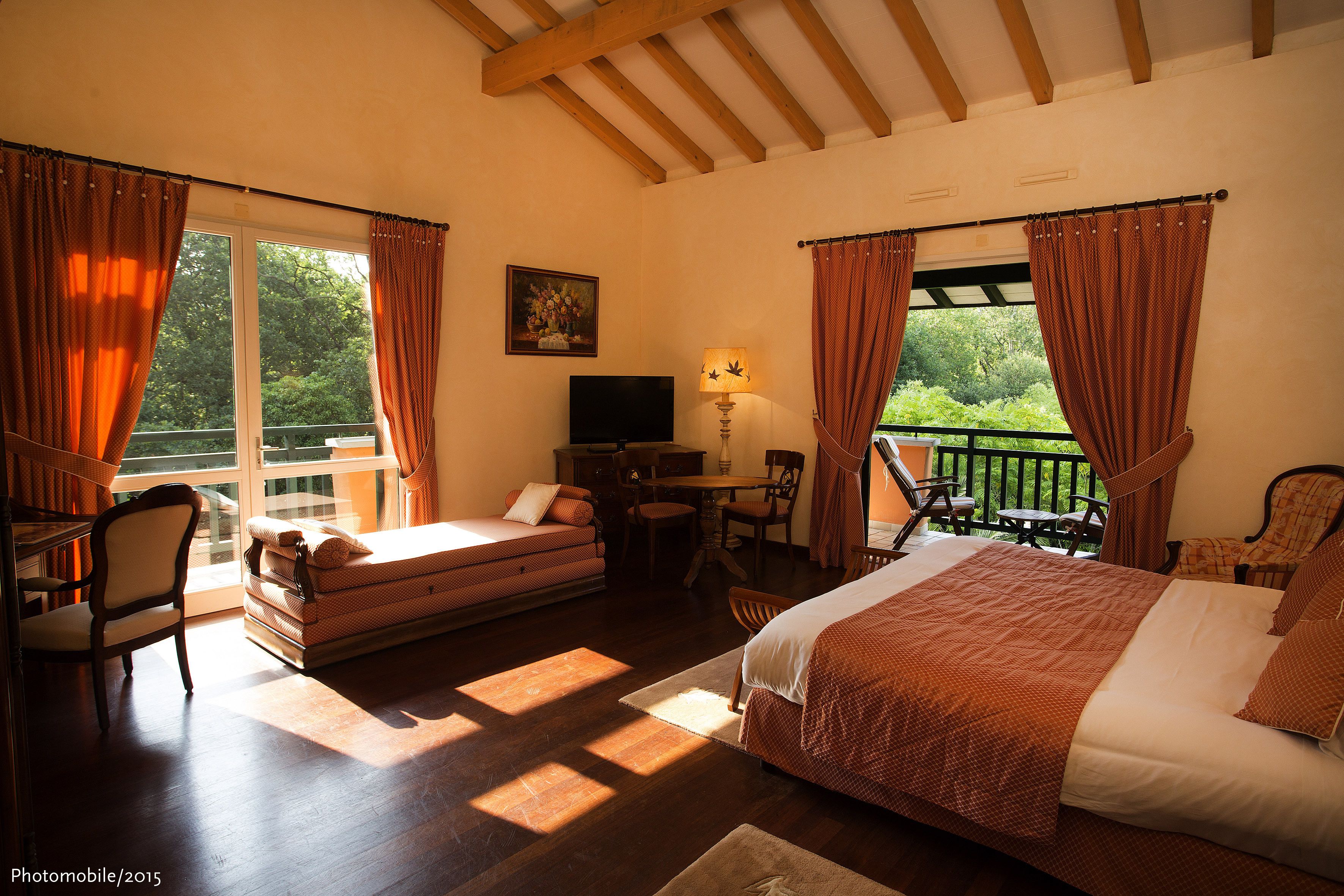 A bedroom with a bed, a desk, a chair, and a sofa. There is a balcony with a table and chairs.